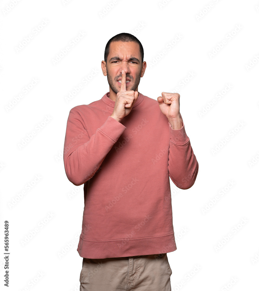 Serious young man asking for silence gesturing with his finger Serious young man asking for silence gesturing with his finger