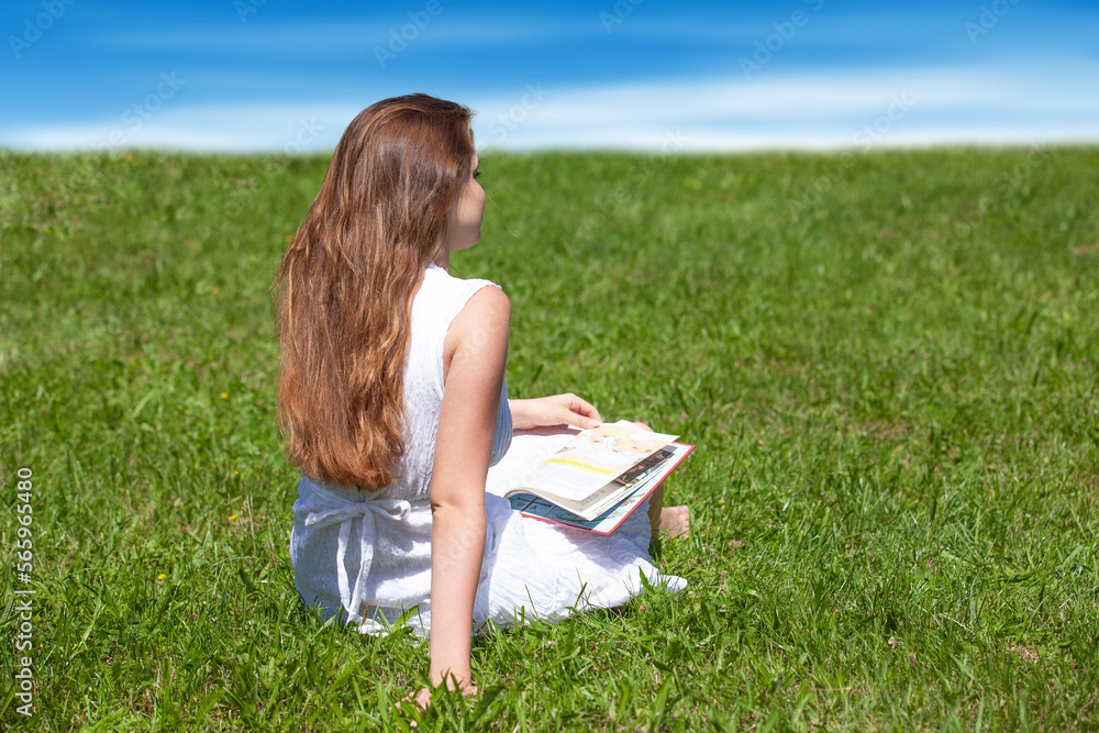 happy female student sitting on the grass with a book happy female student sitting on the grass with a book