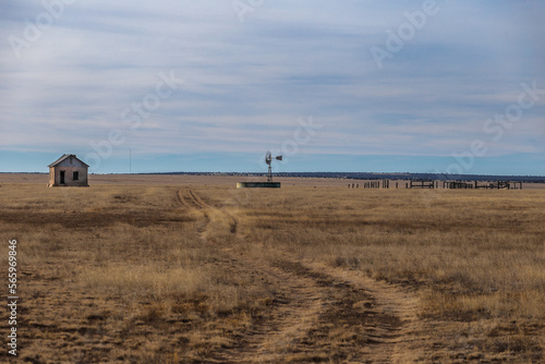 Abandoned homefront with windmill and wooden fencing in yellow grass pasture in rural New Mexico photo