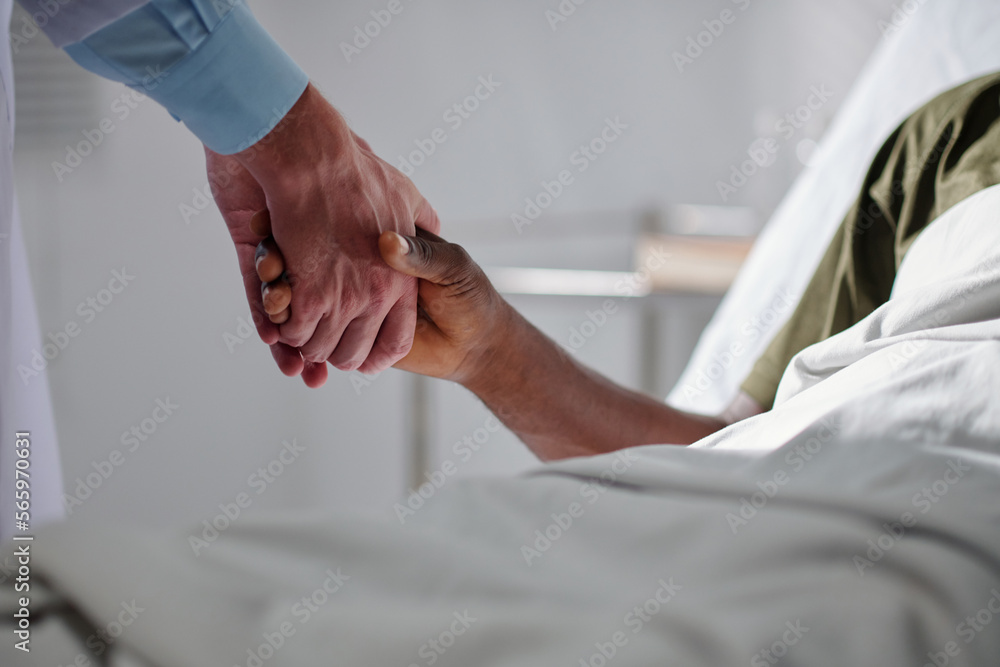 Medical worker shaking hand of sick military man lying on bed in hospital ward