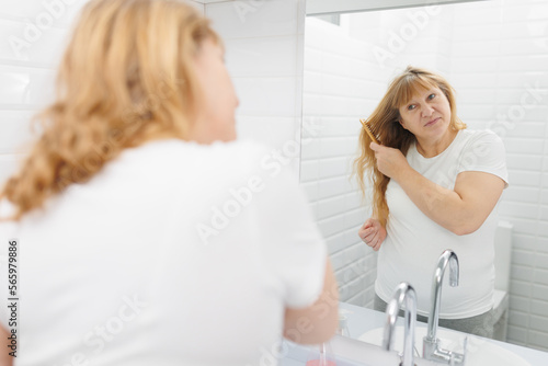 Happy young woman is combing hair in the bathroom.