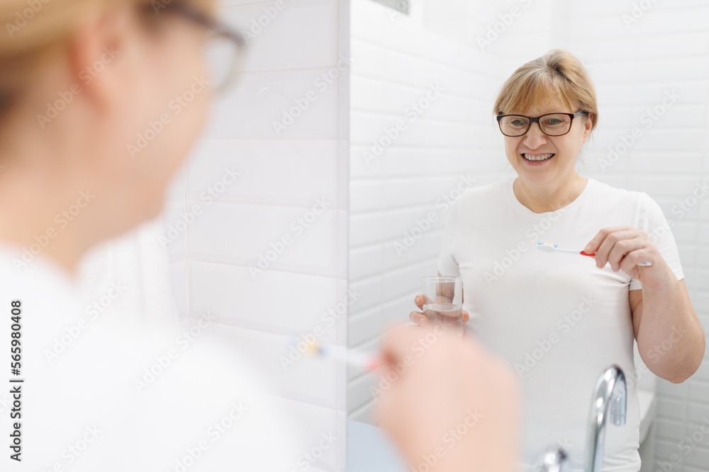 Happy caucasian woman brushing teeth and looking at mirror in bathroom Happy caucasian woman brushing teeth and looking at mirror in bathroom
