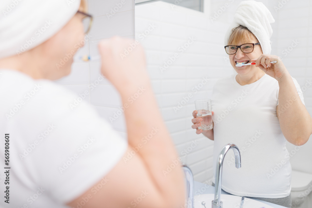 Happy caucasian woman brushing teeth and looking at mirror in bathroom Happy caucasian woman brushing teeth and looking at mirror in bathroom