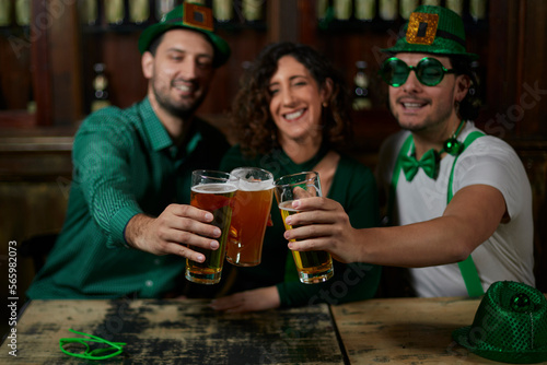 Three friends toasting with beers, in a bar for St. Patrick's Day.