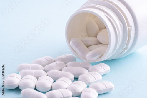 White pills spilling out of pill bottle on white