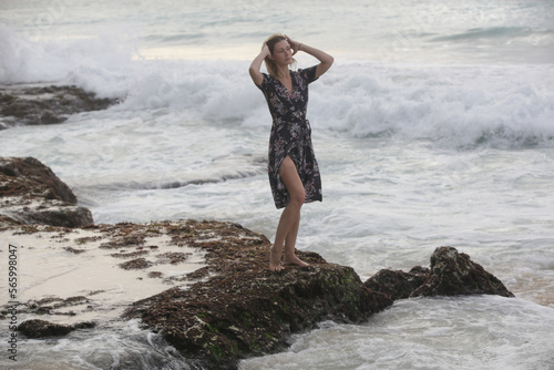 Portrait of beautiful young woman in dark floral wrap dress on wild rocky beach  © triocean