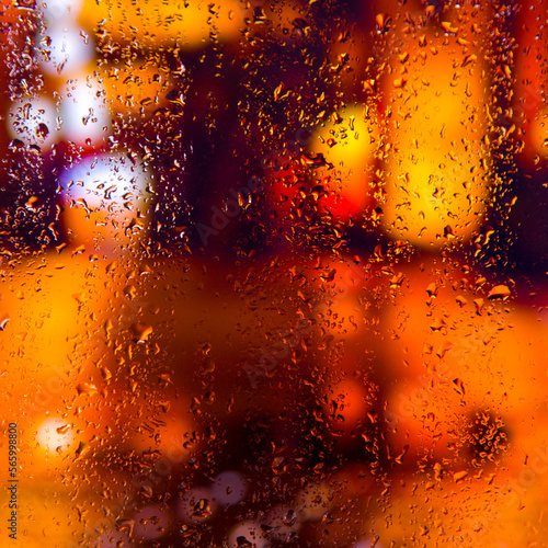 City view through a window on a rainy night Rain drops on window with road light bokeh  City life in night in rainy season abstract background. Focus on drops on glass