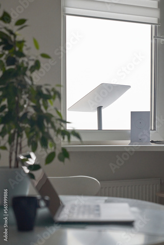 KYIV, UKRAINE - JANUARY 24, 2023: Starlink antenna and wi-fi router on windowsill in home office interior with laptop on table with cup of coffee in foreground, selective focus.