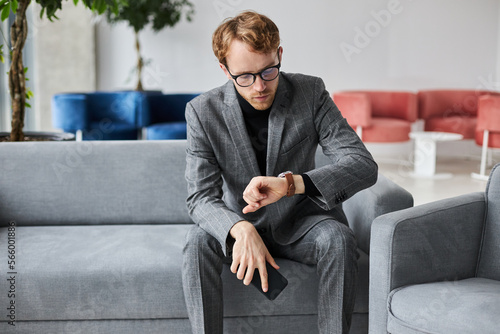Фотография Male entrepreneur in suit, checking time on wrist watch, sitting in armchair in