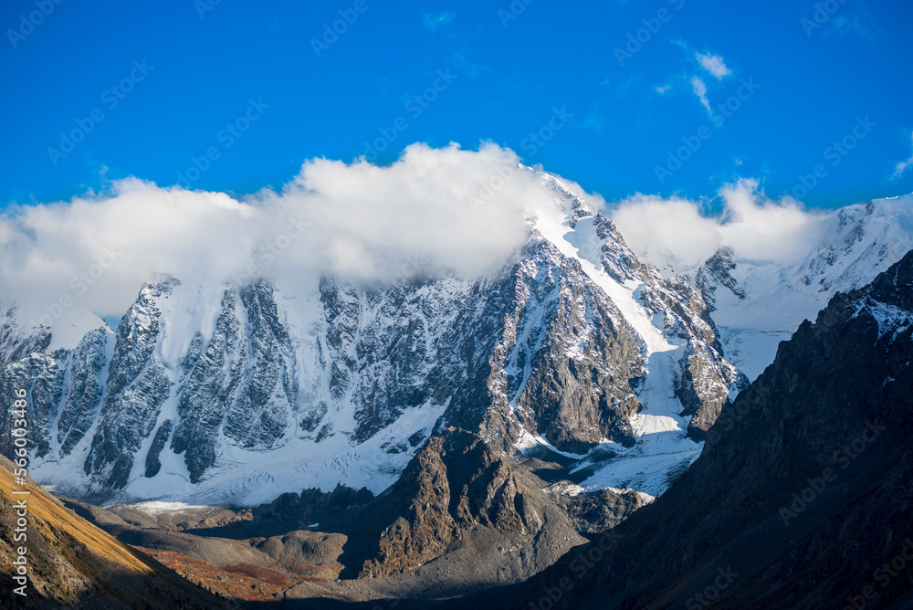 White clouds cover the tops of high rocky mountains with snow and glaciers in Altai on a bright day. Peaks Dream, Fairy Tale, Beauty.