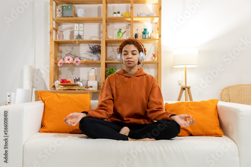 Yoga mindfulness meditation. Young healthy african girl practicing yoga at home. Woman sitting in lotus pose on couch meditating smiling relaxing indoor. Girl doing breathing practice. Yoga at home