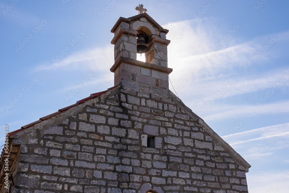 Close up view of stone bell tower of Saint Sava (St Sava) chapel with blue sky background near island Sveti Stefan (St. Stephen) in Bay of Budva, Montenegro, Europe. Sunbeams touching the landmark