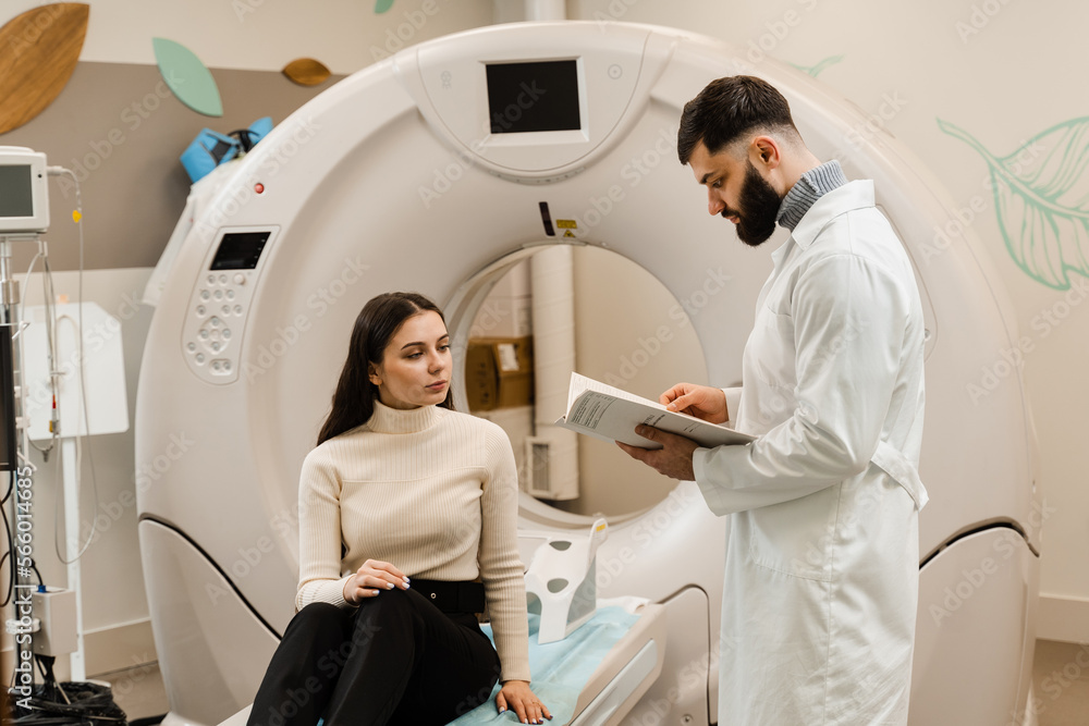 Doctor with woman patient in CT scanning room in medical clinic. Consultation before computed tomography x-ray scan procedure to obtain detailed internal images of girls body. Doctor with woman patient in CT scanning room in medical clinic. Consultation before computed tomography x-ray scan procedure to obtain detailed internal images of girls body.