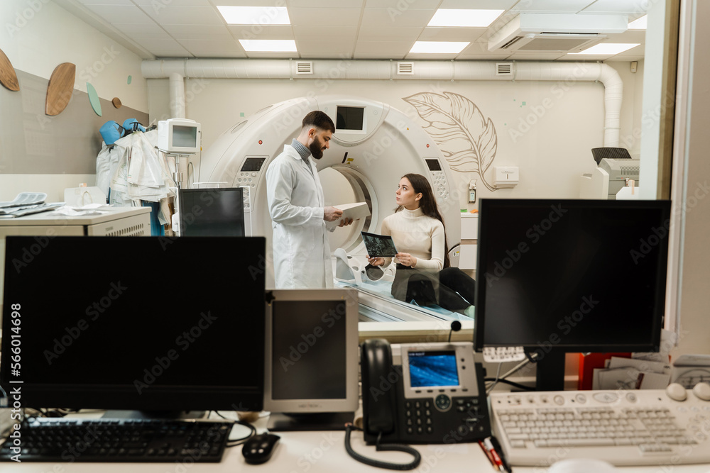CT scan radiologist showing x-ray of brains to girl patient in computed scanning room. CT Doctor consulting patient and showing brains x-ray to patient in computed tomography room. CT scan radiologist showing x-ray of brains to girl patient in computed scanning room. CT Doctor consulting patient and showing brains x-ray to patient in computed tomography room.