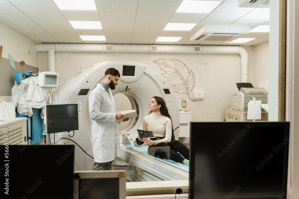 Naklejka premium CT Doctor consulting patient and showing brains x-ray to patient in computed tomography room. CT scan radiologist showing x-ray of brains to girl patient in computed scanning room.