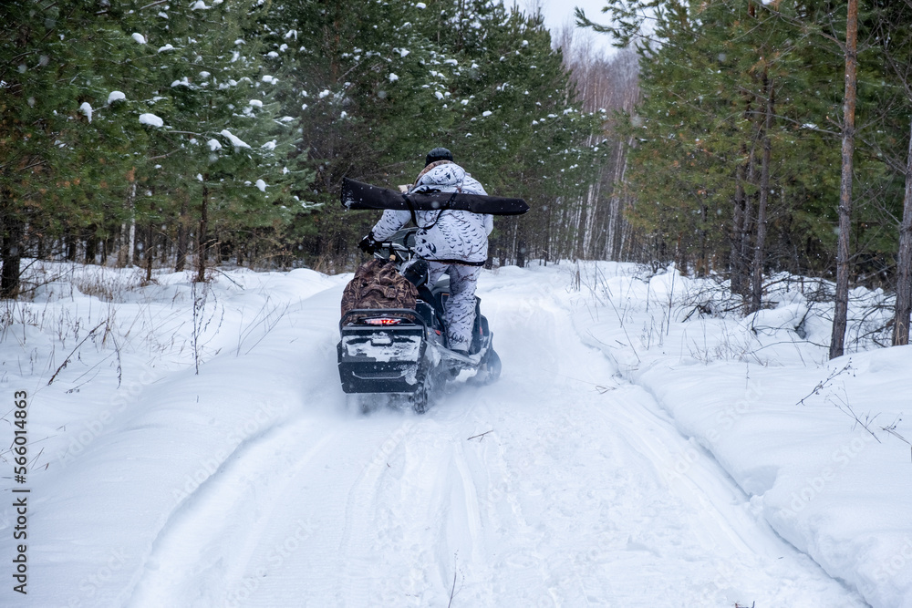 Hunters on snowmobiles ride in the winter forest