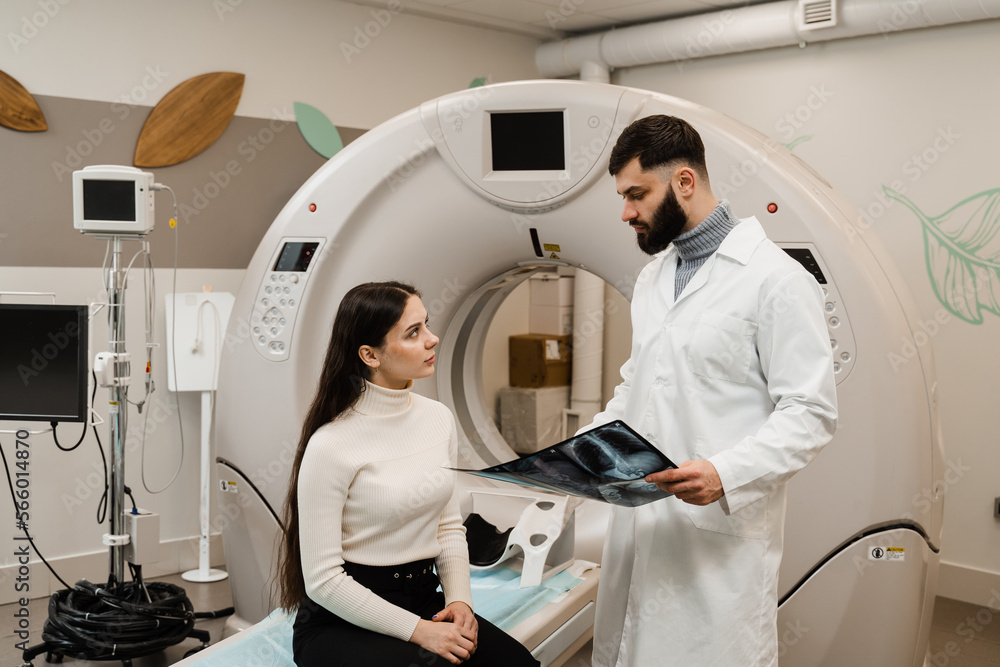 CT scan radiologist showing x-ray of abdomen to girl patient in computed scanning room. CT Doctor consulting patient and showing chest x-ray to patient in computed tomography room. CT scan radiologist showing x-ray of abdomen to girl patient in computed scanning room. CT Doctor consulting patient and showing chest x-ray to patient in computed tomography room.