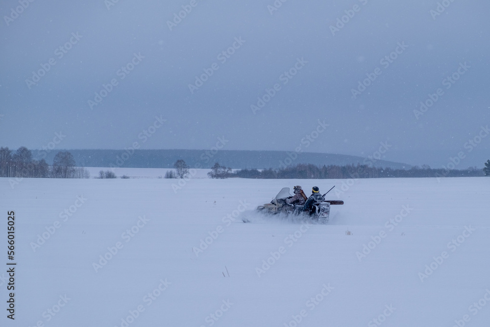 Fototapeta premium Hunters on snowmobiles ride in the winter forest