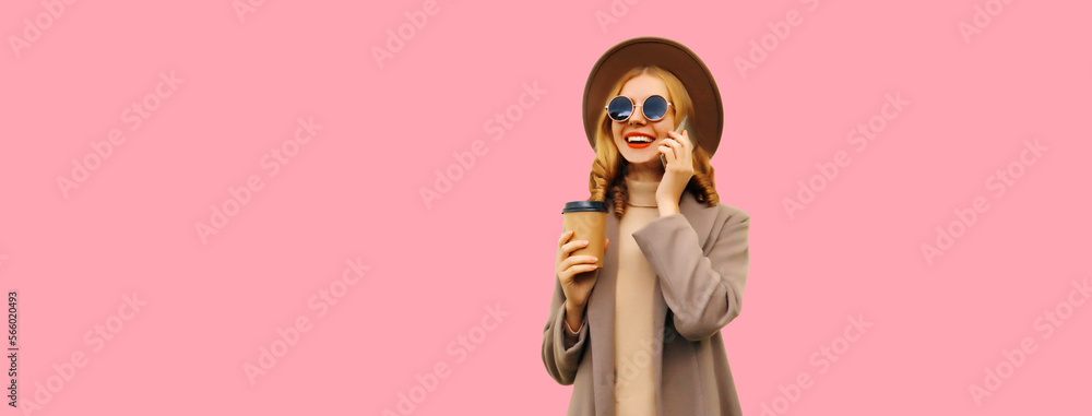 Portrait of beautiful smiling young woman calling on smartphone with cup of coffee wearing brown coat, round hat looking away on pink background, blank copy space for advertising text Portrait of beautiful smiling young woman calling on smartphone with cup of coffee wearing brown coat, round hat looking away on pink background, blank copy space for advertising text
