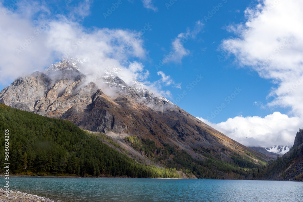 Snowy mountains with glaciers in the distance of the turquoise lake Shavlinskoe surrounded by rocks with snow and fog in Altai. Snowy mountains with glaciers in the distance of the turquoise lake Shavlinskoe surrounded by rocks with snow and fog in Altai.