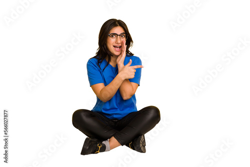 Young indian woman sitting on the floor cut out isolated saying a gossip, pointing to side reporting something.