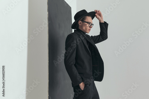 portrait of sexy man in black suit with hand in pocket adjusting hat