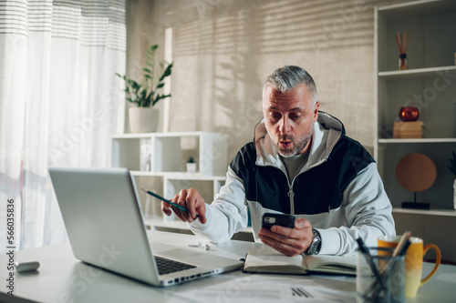 Middle aged man using smartphone and a laptop while working in a home office