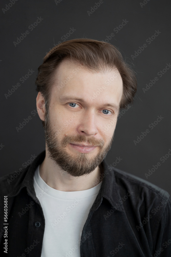 portrait of a man with a beard in a white T-shirt and black shirt on a dark background looks at the camera