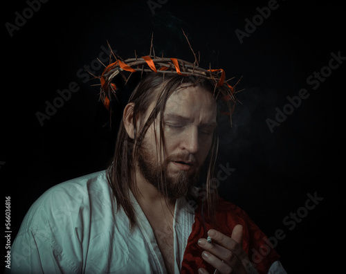 Jesus Christ smokes a cigarette wearing a crown of thorns and white chiton toga cape himation suffering for mankind's sins in artistic portrait photo
