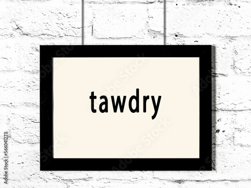 Black frame hanging on white brick wall with inscription tawdry