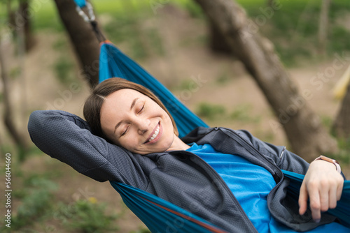 Smiling woman in casual clothes resting in a hammock outdoors in the weekend