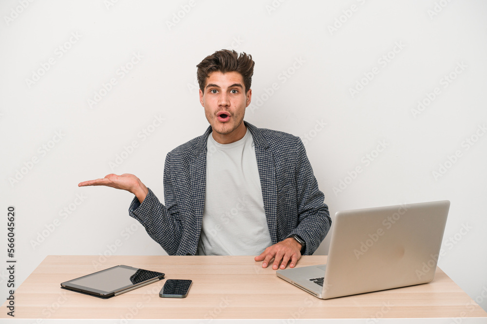 Young entrepreneur man working with a laptop isolated impressed holding copy space on palm. Young entrepreneur man working with a laptop isolated impressed holding copy space on palm.
