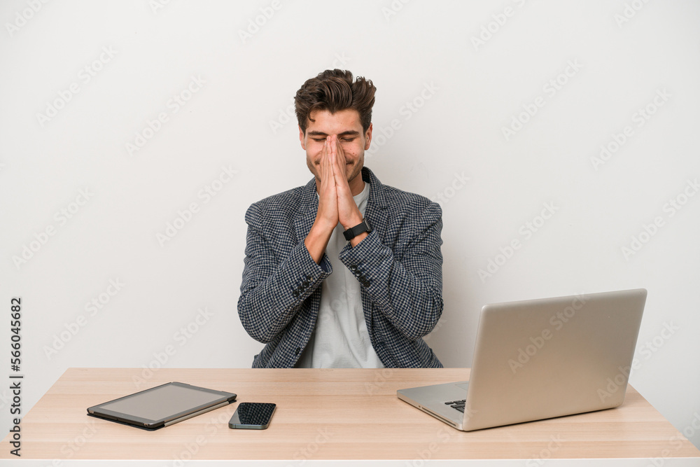 Young entrepreneur man working with a laptop isolated holding hands in pray near mouth, feels confident. Young entrepreneur man working with a laptop isolated holding hands in pray near mouth, feels confident.