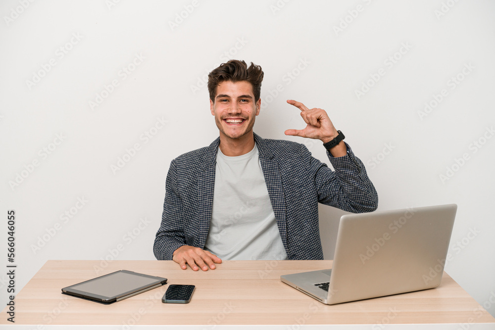 Young entrepreneur man working with a laptop isolated holding something little with forefingers, smiling and confident. Young entrepreneur man working with a laptop isolated holding something little with forefingers, smiling and confident.