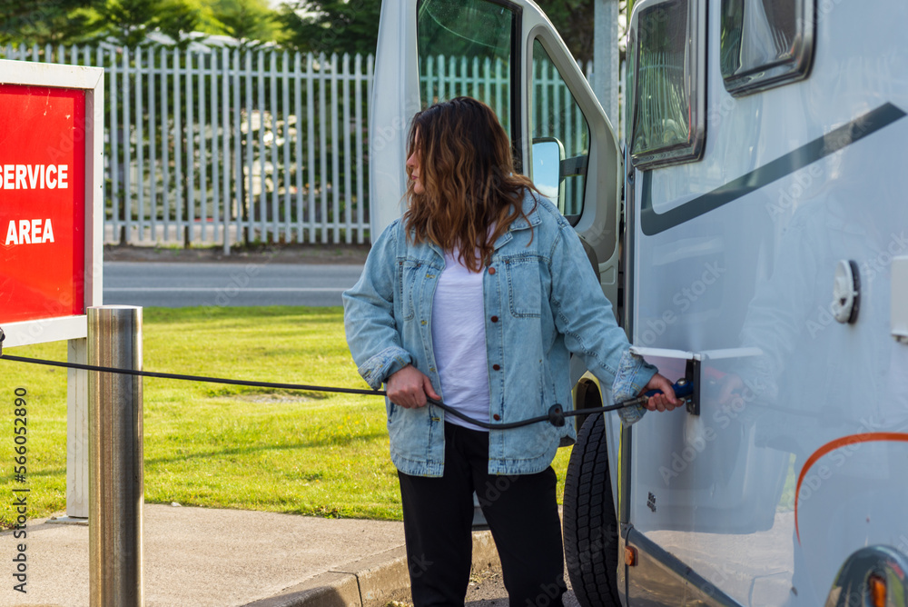 custom made wallpaper toronto digitalmiddle-aged woman with long hair and denim shirt, filling motorhome water tank at a camper service area,