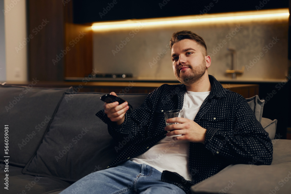 Great TV show.Handsome cheerful young man holding remote control and watching TV while sitting on the couch at home. Great TV show.Handsome cheerful young man holding remote control and watching TV while sitting on the couch at home.