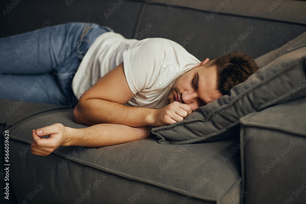 A young man in a white T-shirt, exhausted, fell asleep in front of the TV. Lazy man watching television at night alone.