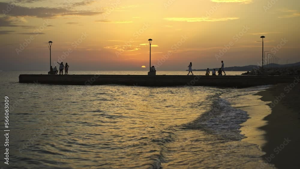 Amazing view of sea waves splashing on the beach sand at sunset. Some tourists spending quality time on the beach Amazing view of sea waves splashing on the beach sand at sunset. Some tourists spending quality time on the beach
