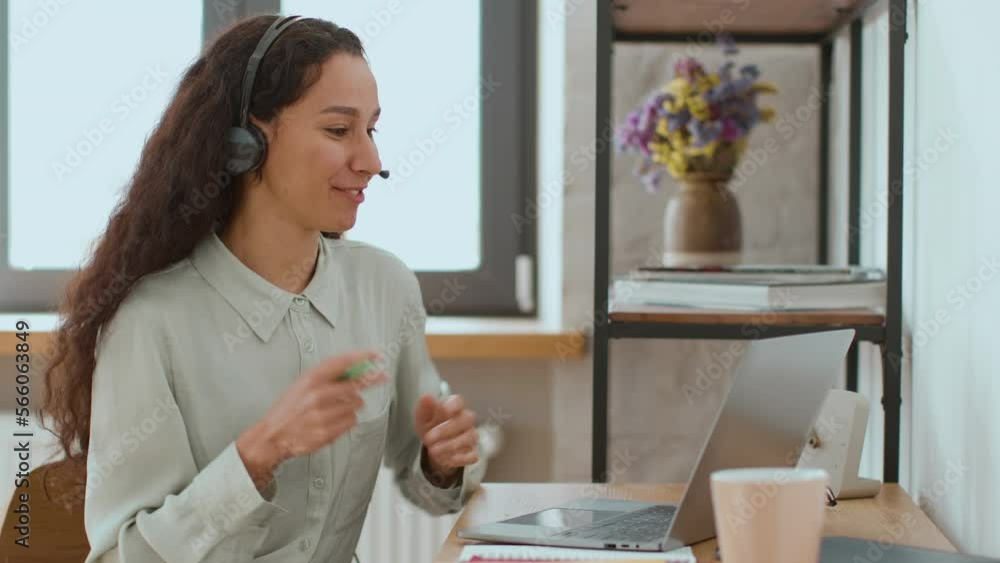 Young professional woman sales agent in headset with mic video chatting with client online via laptop, empty space