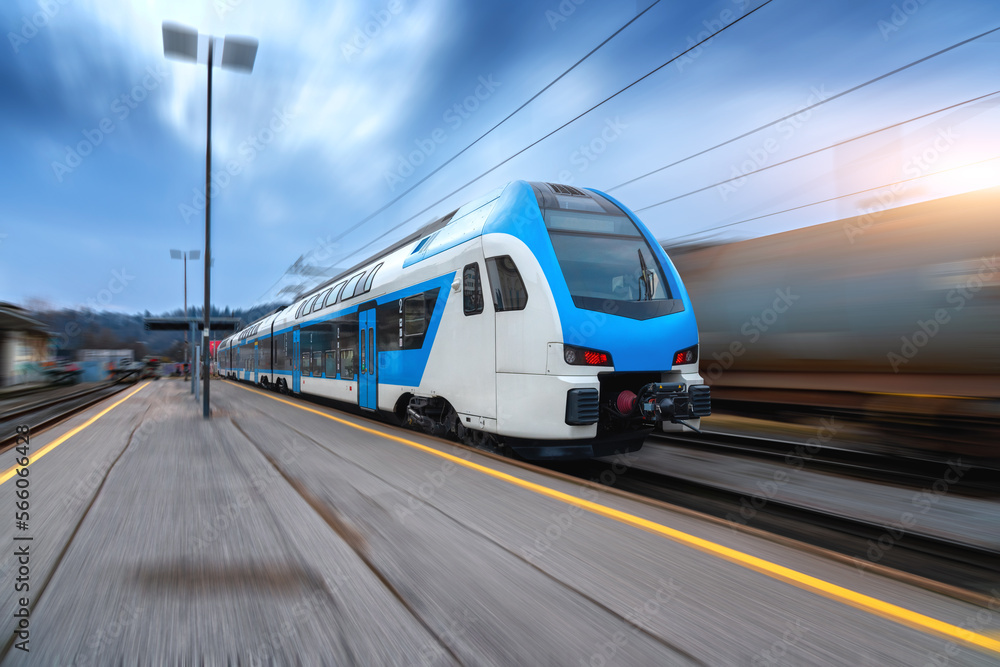 Blue high speed train in motion on the railway station at sunset. Fast modern intercity train and blurred background. Railway platform. Railroad in Slovenia. Commercial and passenger transportation