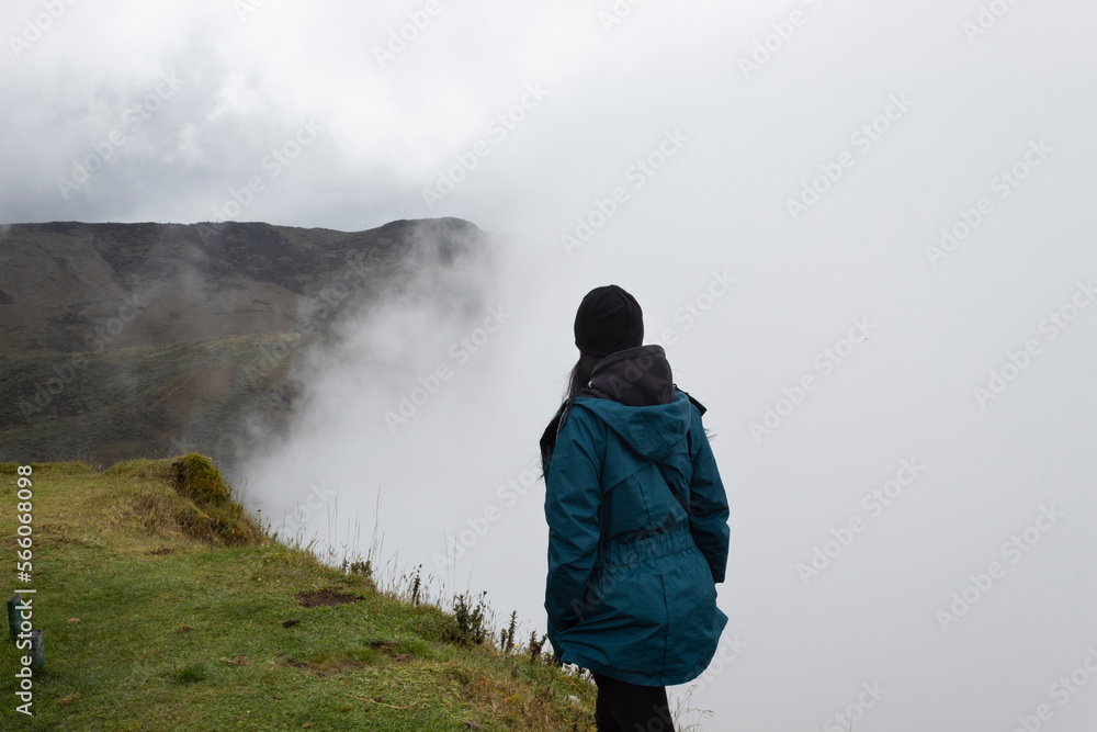 Young woman walking in relax attitude watching cloudy mountain landscape at the edge of a grass hill in colombian paramo Young woman walking in relax attitude watching cloudy mountain landscape at the edge of a grass hill in colombian paramo
