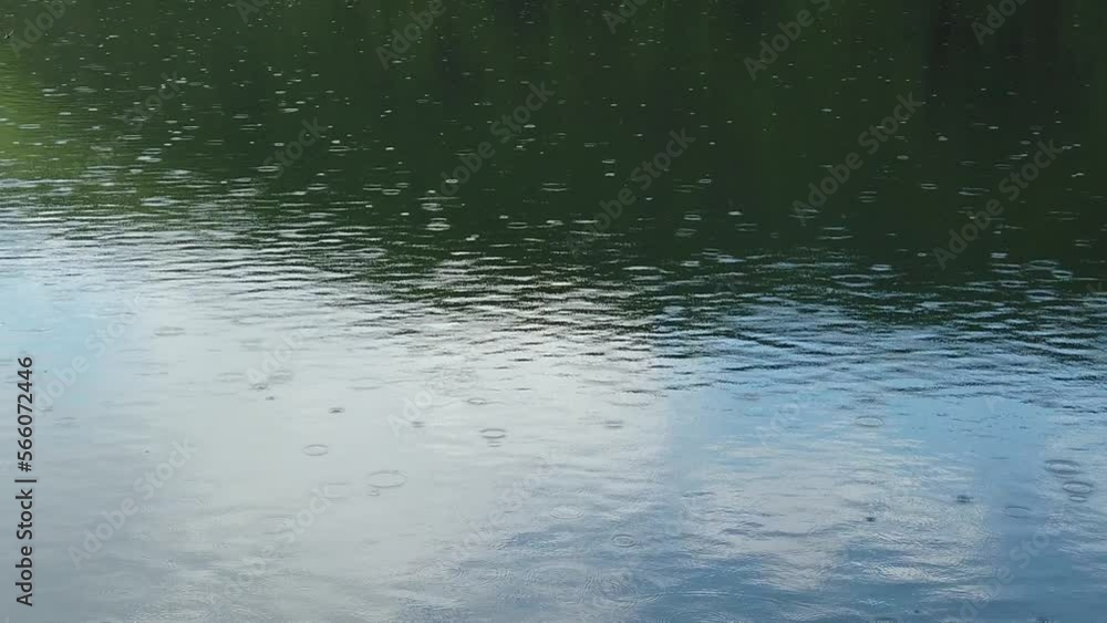 Rain drops falling on the surface of the mountain lake with reflection of the blue sky and green forest Rain drops falling on the surface of the mountain lake with reflection of the blue sky and green forest