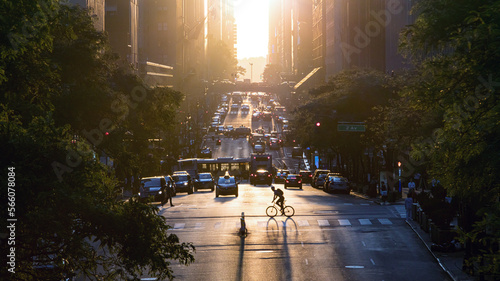 Man riding a bike across the busy intersection past the cars, taxis and buses on 42nd street in Midtown Manhattan, New York City with sunset background photo