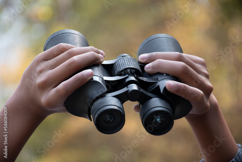 Hands holding binoculars, blurred natural background, concept for vacation, observation, trekking, camping, hiking and birdwatching. © Sophon_Nawit
