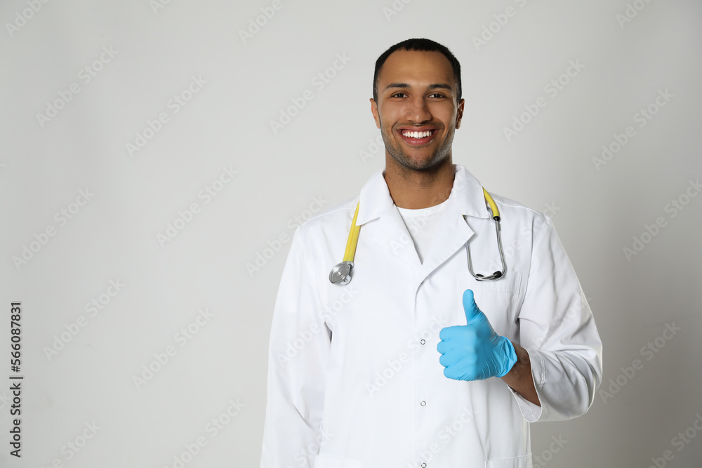 Doctor or medical assistant (male nurse) in uniform showing thumb up on light grey background. Space for text Doctor or medical assistant (male nurse) in uniform showing thumb up on light grey background. Space for text