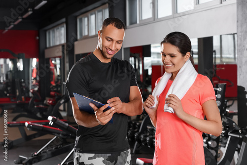 Happy trainer showing woman workout plan in modern gym, space for text