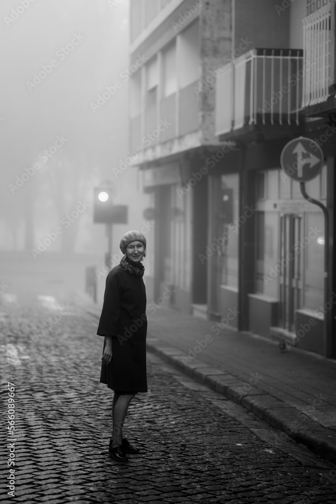 A woman on the sidewalk in the thick fall morning fog. Black and white photo.