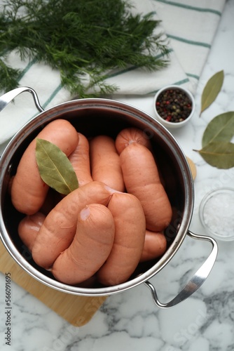 Pan of delicious sausages, dill, bay leaf, pepper and salt on white marble table, flat lay photo