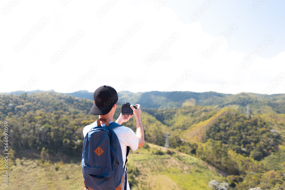 Traveler man on top of a mountain and taking pictures or recording video with his professional camera of the landscape.