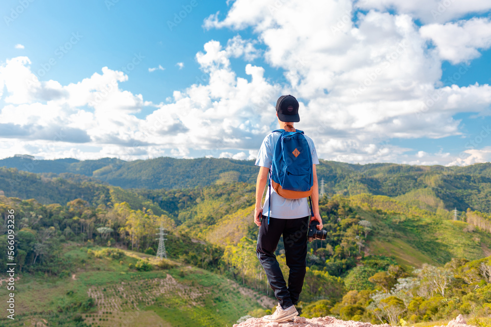 Traveler standing on the top of the mountain and holding a professional camera while contemplating the green mountains landscape. Traveler standing on the top of the mountain and holding a professional camera while contemplating the green mountains landscape.